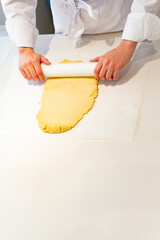 A pastry chef is rolling out dough on a table with a rolling pin. yellow dough and the worker is...