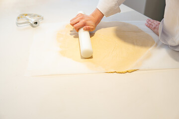 photograph of two chef's hands rolling out cake dough between non-stick baking papers with the help of a rolling pin.