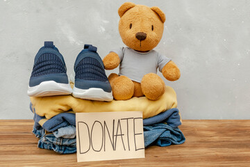 Stack of old baby children clothes,teddy bear toys,sorted into Donate.Donation,volunteering help,humanitarian aid.charity on gray background.Recycle clothing,eco cotton