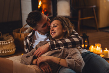 Concept of happy family relationships between man and woman. Young couple relaxed near fireplace in...