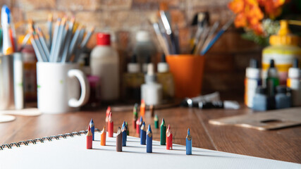 Small colored pencils on white paper on a wooden table with art supplies in the background