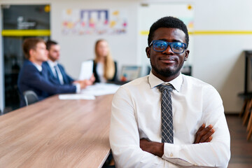 Confident African corporate professional in formal workwear sits at meeting table, focus on...