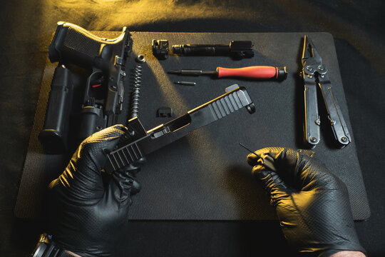 Cleaning and repairing weapons. Hands of a gunsmith and a disassembled pistol g19 in a workshop.