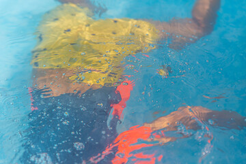 Abstract underwater view of a child swimming, with vivid reflections and rippling colors in a pool.