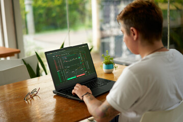 Focused crypto trader analyzes market data on laptop screen in modern coworking space. Person...