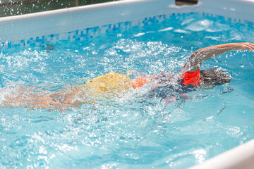 Child in a swimming pool, arm extended, navigating the water with yellow and orange floaties