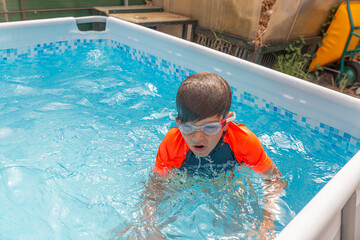 Boy in pool catching breath after swimming, water droplets around as he surfaces in a sunny...