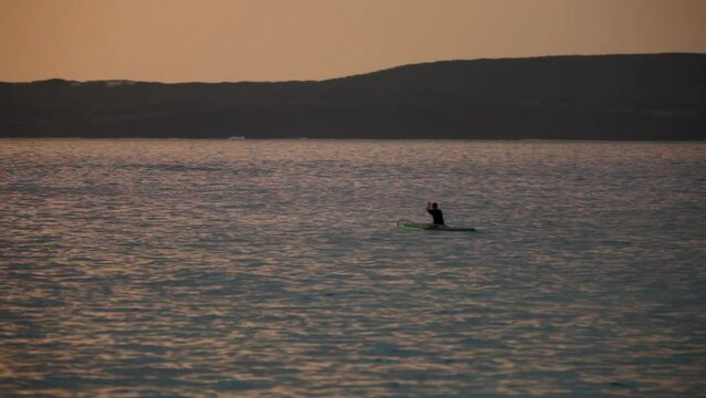 Silhouette of man paddling canoe in ocean at dusk