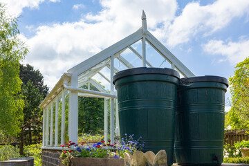 Two green water butts outside a greenhouse being used for water storage, water collection system in...