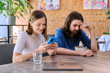 Young people, couple man and woman relaxing together in cafe, using smartphone