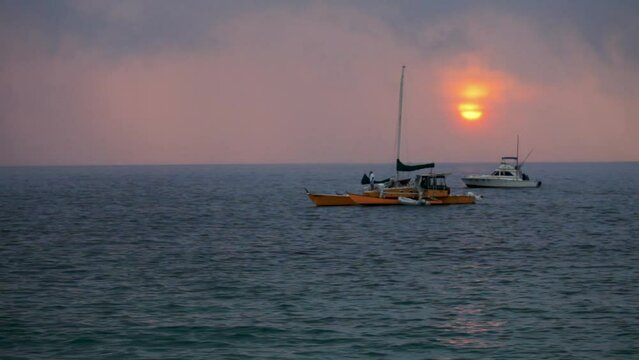 Beautiful red sun in overcast sky and boats in ocean