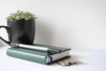 Green notepad, black cup with green branches, pen and money on a white background. Background, copy, space for text