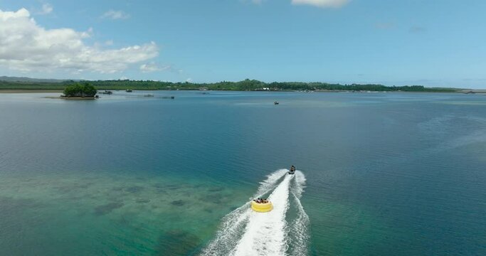 Drone following the Jet Ski over blue sea dragging a watercraft with tourist. Britania Islands. Surigao del Sur, Philippines.