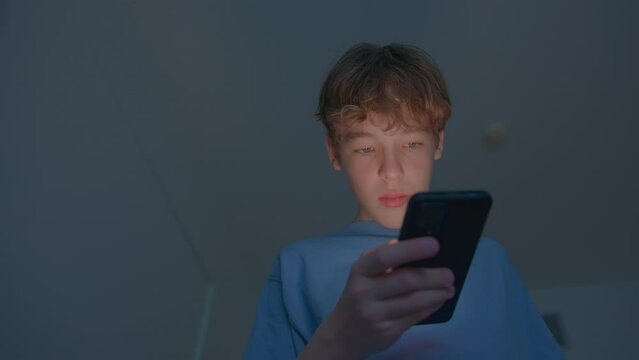 Teen boy engrossed in smartphone screen, blue light illuminating his face