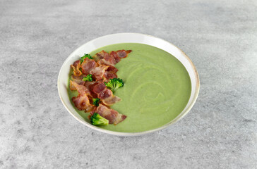 Creamy broccoli soup with bacon on a gray background. 