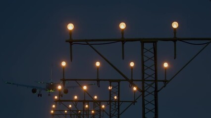 The plane descends, flying past the bright lights of the runway in the evening
