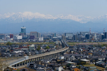 Obraz premium 満開の桜春霞の北アルプス立山連峰と北陸新幹線の見える富山市街地