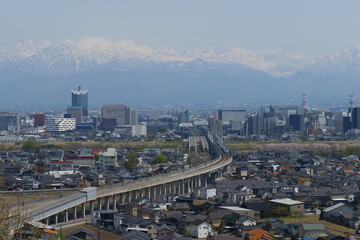 満開の桜春霞の北アルプス立山連峰と北陸新幹線の見える富山市街地