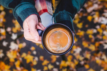 Female hand holding a cup of fresh brewed coffee with yellow leaves on the background
