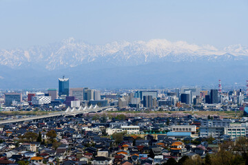 満開の桜春霞の北アルプス剱岳立山連峰と北陸新幹線富山市街地