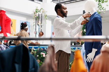 Clothing store employee adjusting male suit on mannequin while working in shopping mall. Fashion...