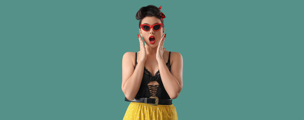 Shocked young pin-up woman in sunglasses on green background