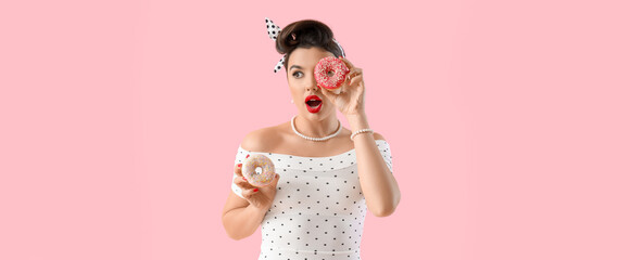 Shocked young pin-up woman with tasty donuts on pink background