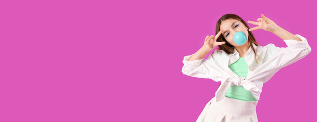Trendy girl blowing bubble gum while showing victory gestures on purple background