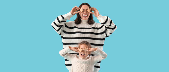 Funny mother and her little daughter with tasty cookies on blue background