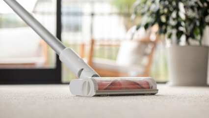 A cordless vacuum cleaner cleans the carpet on the floor. Cleaning and cleaning. Close-up
