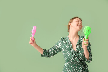 Beautiful young woman with handheld mini fans on green background © Pixel-Shot