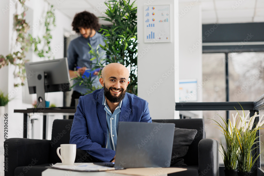 Poster smiling business entrepreneur working on laptop and looking at camera in start up company office. su