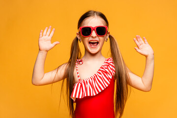 A happy little girl in a red swimsuit laughs cheerfully and showing her palms hands on yellow...
