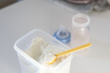 Dry powder formula milk for feeding babies in a can with yellow plastic scoop and empty feeding bottle