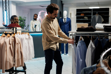 Young man customer examining apparel options in clothing store department while choosing formal...