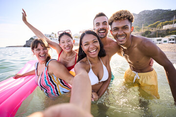 Portrait of a group of happy diverse young people in swimwear smiling and taking a selfie inside...