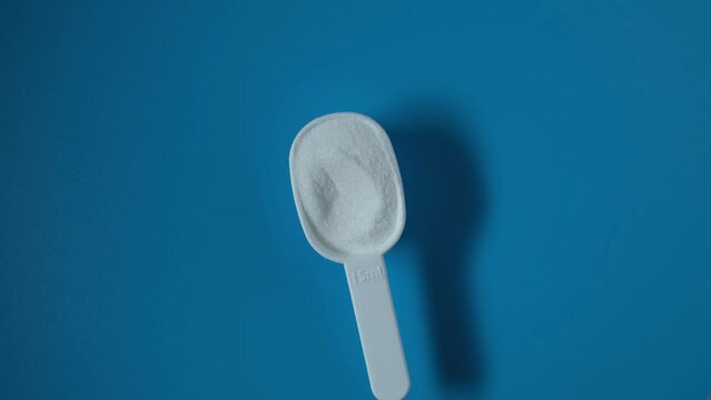Sodium erythorbate or isoascorbate powder in measuring scoop on blue background, top view. Food additive E316 used predominantly in meats, poultry, and soft drinks. Sodium salt of erythorbic acid.