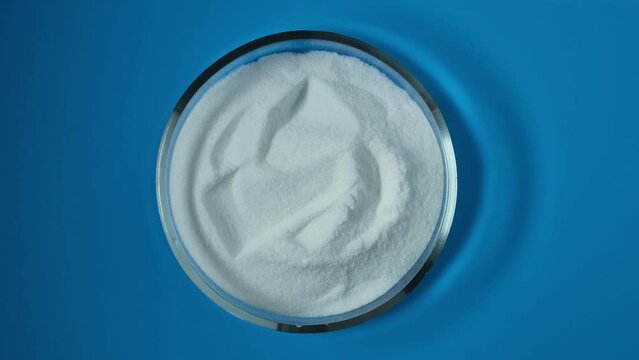 Food additive E316 in Petri dish, top view. Counterclockwise rotation. Sodium erythorbate or isoascorbate powder used in food industry, predominantly in meats, poultry, and soft drinks.