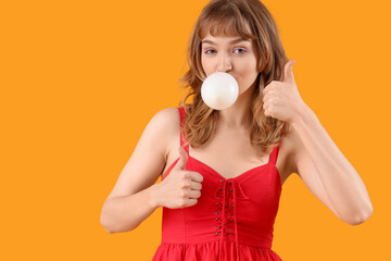 Beautiful young woman with chewing gum showing thumbs-up on yellow background