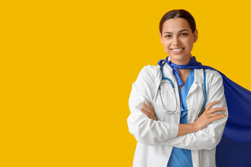 Beautiful female doctor in superhero costume on yellow background