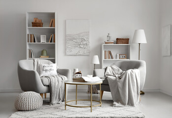 Interior of light living room with cozy armchairs and books on coffee table