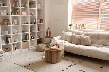 Interior of light living room with cozy sofa, wooden coffee table and bookshelves