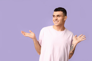Handsome ashamed young man shrugging on lilac background