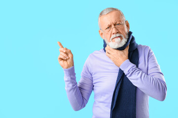 Ill old man with sore throat pointing at something on blue background