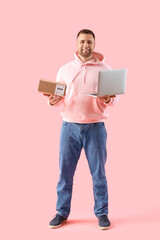 Young man with parcel and laptop on pink background