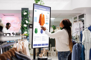 Woman buyer selecting clothes on board, using interactive touch screen monitor in clothing store....