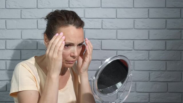 Woman with imperfection on face against mirror. A woman try to see her wrinkles in the mirror.