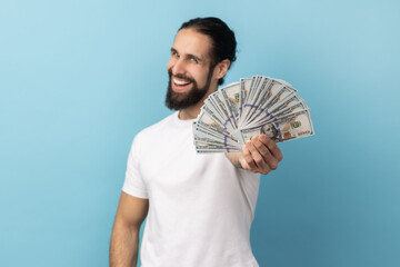 Portrait of happy delighted happy man with beard wearing white T-shirt holding out dollars...
