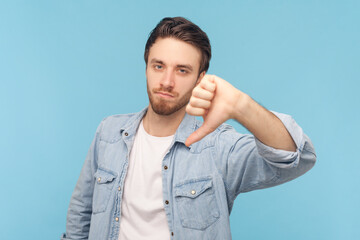 Portrait of sad disappointed unshaven man showing his thumbs down, looking at camera with frowning...