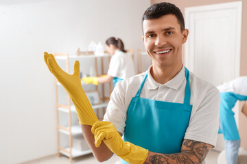 Male worker of cleaning service with rubber gloves in bedroom